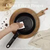 A hand is cleaning a frying pan with a wipe, placed on a wooden board. There are spices scattered around. Voir les images du produit