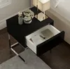 A modern black nightstand with a drawer pulled open, containing a laptop, watch, and notebooks. Produktbild-Vorschau