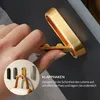 A hand is shown interacting with a gold folding hook mounted on a dark gray surface. A circular inset image shows three hooks (black, gold, and silver) with a handbag being hung on the gold one. Text in German is present. Produktbild-Vorschau