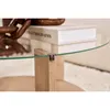 A close-up view of a glass coffee table with a wooden leg and a decorative chain on top. Produktbild-Vorschau