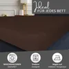 A close-up of a brown fitted sheet on a bed, with marketing icons and text at the bottom. Produktbild-Vorschau
