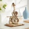 A wooden mechanical cello model is displayed on a desk, stacked on books, with decorative elements and gears visible. Voir les images du produit
