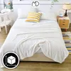 A white textured blanket is draped over a bed with two pillows and a yellow and white striped decorative pillow. Náhled obrázku produktu