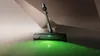 A cordless vacuum cleaner head with a green light illuminating the floor, showing dust particles being picked up. Podgląd zdjęcia produktu