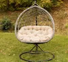 A hanging egg chair with a beige cushion sits on a grassy lawn with fallen leaves and trees in the background. Produktbild-Vorschau