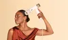 A woman is using a white hairdryer on her hair. Voir les images du produit