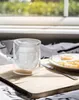 A double-walled glass with a Stormtrooper helmet design inside, placed on a wooden tray next to a plate of fried eggs and a knife. The background shows a sunlit window. Anteprima dell’immagine prodotto