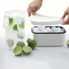 A person's hands are shown placing the lid on an ice cube box filled with ice cubes. A pitcher of iced drink with lime and mint is to the left, and limes are in the foreground. Podgląd zdjęcia produktu