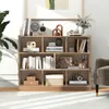 A wooden bookshelf filled with books and decorative items, placed in a well-lit room with a plant and a chair. Produktbild-Vorschau