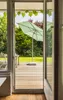 View of a garden through an open door, featuring a patio umbrella and outdoor furniture. Produktbild-Vorschau