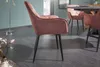 A pink velvet armchair with dark metal legs is positioned diagonally in a room with a teal wall and a grey wooden floor. Another similar chair and a dining table are visible in the background. Produktbild-Vorschau