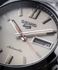 A close-up view of a watch face, showing the brand logo, hands, and date display. Produktbild-Vorschau