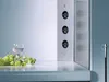 A corner electrical outlet with three sockets, placed on a countertop next to a bunch of grapes and a glass of white wine. Produktbild-Vorschau