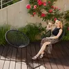 A woman sits in a garden chair on a wooden deck, with a rose bush in bloom behind her. Náhled obrázku produktu