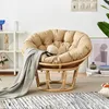 A papasan chair with a cushion and a blanket, placed in a room with shelves and a rug. Produktbild-Vorschau