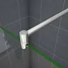 Close-up view of a shower enclosure corner with a silver metal support bar and a green strip on the glass. Produktbild-Vorschau