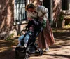 A woman pushing a stroller with a baby in it on a sunny day. Produktbild-Vorschau