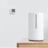 A white humidifier and a small digital thermometer are displayed on a wooden surface against a white wall. Podgląd zdjęcia produktu