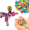 A pink camouflage gel blaster gun with a hopper full of colorful gel balls, and a hand holding a pile of gel balls. Náhled obrázku produktu