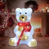 A festive Christmas teddy bear decoration with lights, set against a cozy fireplace background. Voir les images du produit