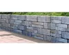 A stone wall with a patio in front and greenery behind. Produktbild-Vorschau