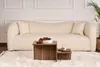 A cream-colored sofa with two pillows is in the background, with a wooden coffee table in front of it. A small plant in a basket is visible on the right side. Náhľad obrázku produktu
