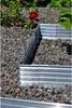 A close-up view of a raised garden bed made of corrugated metal, surrounded by gravel and with a red rose in the background. Produktbild-Vorschau