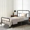 A bedroom scene with a black metal bed frame, bedding, and a nightstand. Náhled obrázku produktu