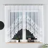 A white lace curtain with a scalloped bottom edge hangs over a window. The window shows a dark, blurry outdoor scene. A wooden windowsill below the window holds a small potted plant, a framed picture, and a lantern. Produktbild-Vorschau