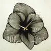 A black metal wall clock shaped like a flower with gold hands. Produktbild-Vorschau