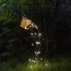 A solar-powered watering can light string in a garden at night. Produktbild-Vorschau