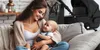 A mother is holding her baby on a couch, with a stroller and diaper bag in the background. Produktbild-Vorschau