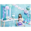 A young girl sits on the floor at a mermaid-themed party, holding a drink. Produktbild-Vorschau