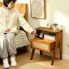 A woman sitting on a bed next to a wooden nightstand. Náhled obrázku produktu