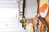 A white electric pot is shown on a wooden table, surrounded by plates of food and vegetables. Produktbild-Vorschau