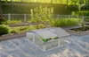 A small greenhouse with plants inside, placed in a garden setting with raised garden beds in the background. Náhled obrázku produktu