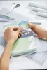 Hands applying a protective film to a book on a cutting mat. Produktbild-Vorschau