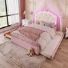 A child's bedroom with a pink upholstered bed featuring a tufted headboard with LED lighting and a crown accent, a pull-out trundle bed, and a teddy bear on a rug. Náhled obrázku produktu
