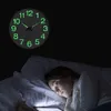 A young girl sleeps in bed next to a glowing wall clock. Voir les images du produit