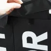 A close-up of a black laundry basket with white lettering, showing a hand interacting with a velcro closure. Náhled obrázku produktu