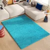 A turquoise shaggy rug is placed on a light wood floor in front of a modern white sectional sofa. Produktbild-Vorschau