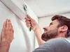A man is using a wrench to tighten a bolt on a wall. Produktbild-Vorschau