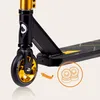 A close-up view of the front wheel and deck of a black and gold stunt scooter. An orange arrow points from the wheel to a circular graphic showing two scooter wheels. Anteprima dell’immagine prodotto