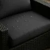 Close-up of a dark gray cushion with water droplets on it, resting on a woven base. Voir les images du produit