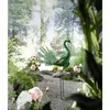 A decorative metal peacock sculpture in a garden setting with flowers and gravel. Produktbild-Vorschau