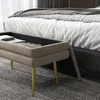 A beige upholstered storage bench with gold legs is placed in front of a bed in a bedroom. Anteprima dell’immagine prodotto