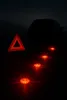 A car's hazard lights and warning triangle are set up on a dark road at night. Podgląd zdjęcia produktu