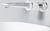 A modern chrome faucet mounted on a light gray wall above a white sink. Produktbild-Vorschau