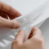 Hands are shown fastening buttons on a white fabric. Produktbild-Vorschau