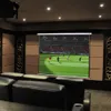 A home theater room with a projector screen displaying a soccer game, and black leather seating in the foreground. Produktbild-Vorschau